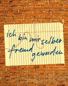 "Ich bin mir selber fremd geworden" Schriftzug auf gelbem Zettel vor roter Ziegelwand